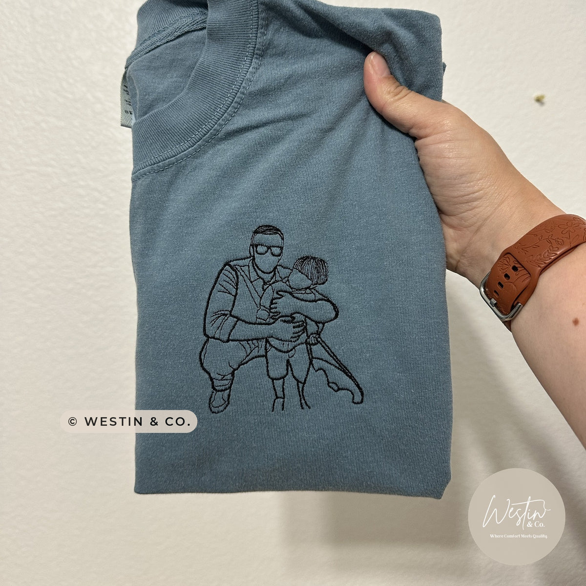 Custom embroidered line art portrait of a dad hugging his son on a blue tee